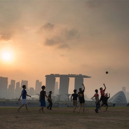 黃昏時分(fēn)，一群男孩在濱海堤壩 (Marina Barrage) 上踢足球，遠(yuǎn)處是濱海灣的朦胧輪廓