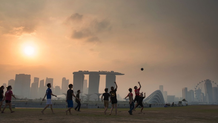 黃昏時分(fēn)，一群男孩在濱海堤壩 (Marina Barrage) 上踢足球，遠(yuǎn)處是濱海灣的朦胧輪廓