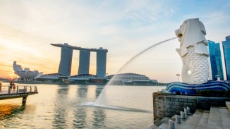 白天，魚尾獅往新(xīn)加坡河 (Singapore River) 噴出水流，背景是新(xīn)加坡天際線(xiàn)